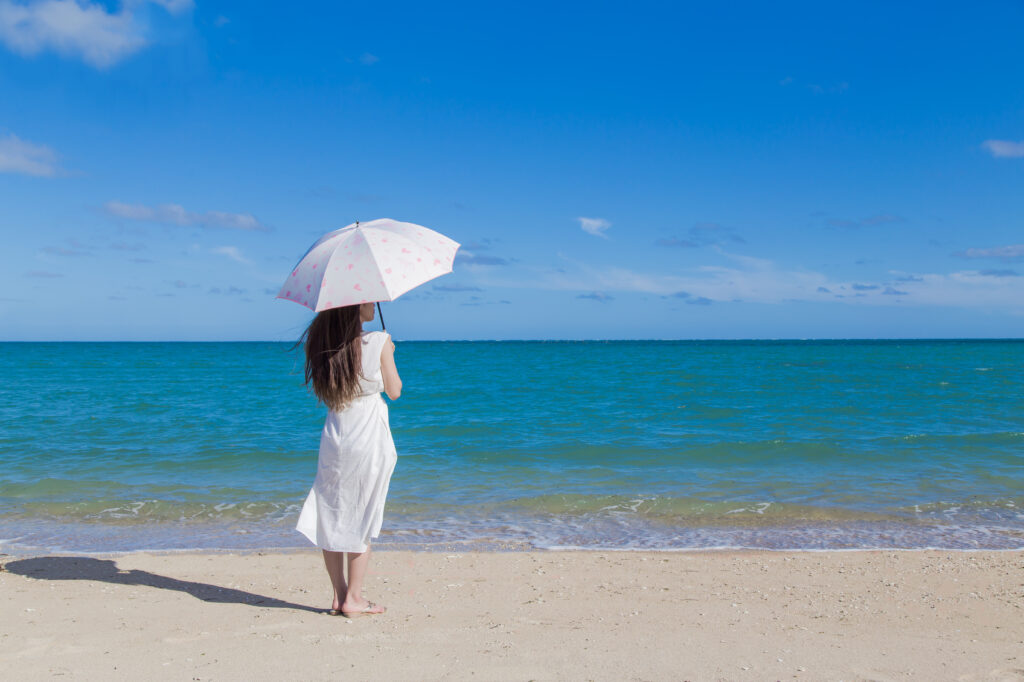 日傘をさした女性が海を眺めている様子